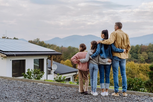 Family admiring there home with solar panels on the roof and mountains in the background